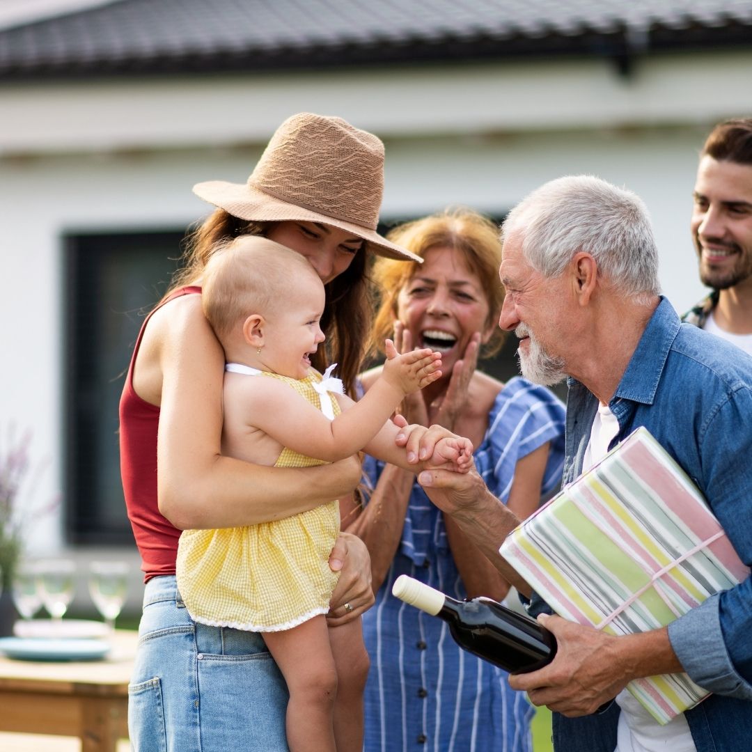 Family members smiling together outdoors as a baby reaches toward an older man.